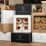 Premium Custom Bakery Boxes with Windows showing detailed textures and structurally rigid designs, featuring The Boxology.US branding in a bustling American bakery. Includes white, kraft, and black samples