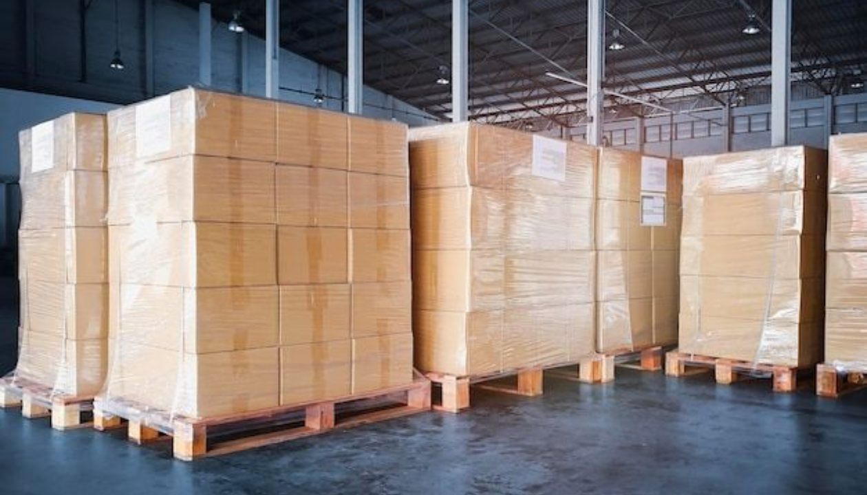 Stacked corrugated shipping boxes on pallets inside a modern warehouse packaging supplier facility.
